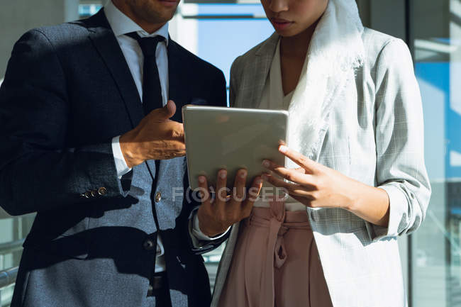 Parte média dos empresários que trabalham em conjunto no tablet digital no corredor do escritório moderno . — Fotografia de Stock