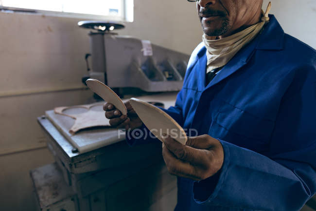 Вид сбоку средневековый афроамериканец, работающий на заводе по производству мячей для крикета, с кожаными вырезанными фигурами, которые он подготовил . — стоковое фото