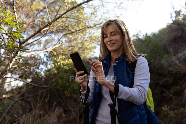 Front view close up of a mature Caucasian woman using a smartphone during a hike with Nordic walking sticks — Stock Photo