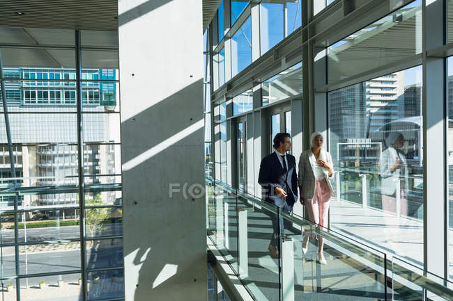 Frontansicht von Geschäftsleuten, die miteinander interagieren, während sie im Flur moderner Büros gehen. — Stockfoto