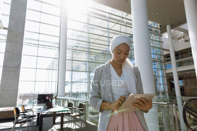Vue de face de femme d'affaires en hijab travaillant sur tablette numérique dans un bureau moderne . — Photo de stock