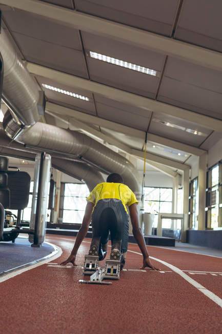 Вид сзади афроамериканского спортсмена-инвалида на стартовом блоке на беговой дорожке в фитнес-центре — стоковое фото