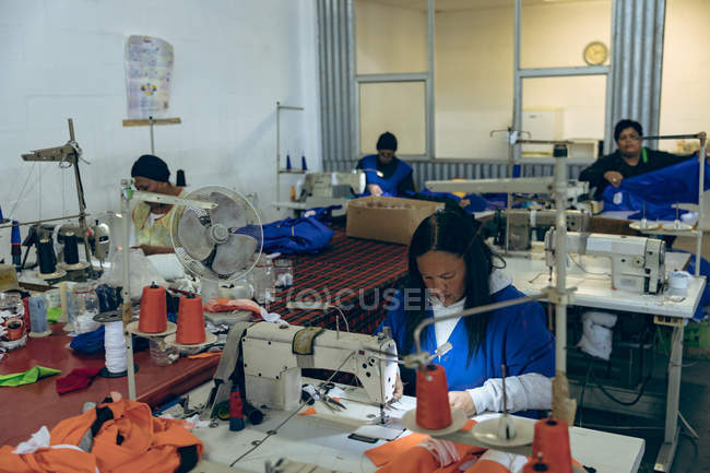 Підвищений вигляд різноманітної групи жінок, які сидять і працюють на швейних машинах на фабриці спортивного одягу . — стокове фото
