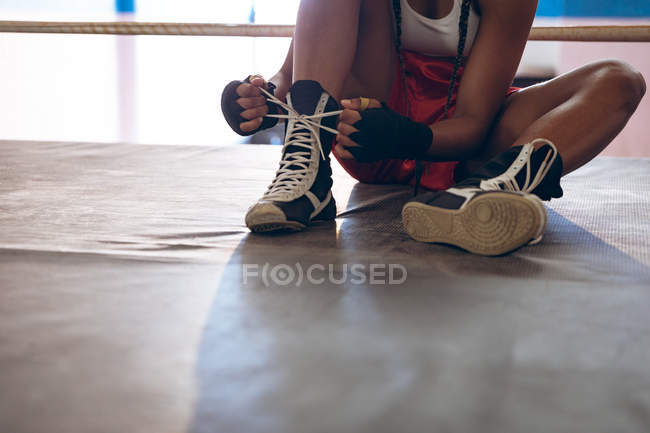 Close-up of female boxer tying shoelaces in boxing ring at fitness center. Strong female fighter in boxing gym training hard. — Stock Photo