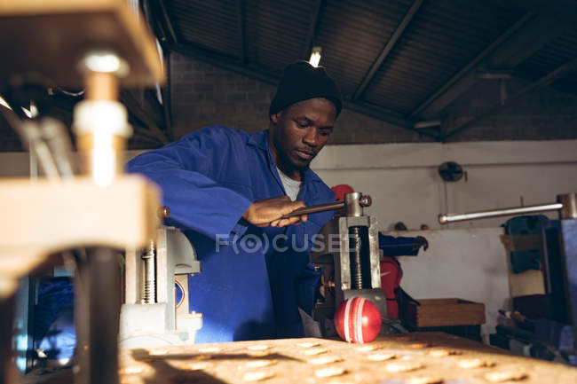 Vue de face gros plan d'un jeune Afro-Américain conduisant une machine dans un atelier d'une usine fabriquant des balles de cricket . — Photo de stock