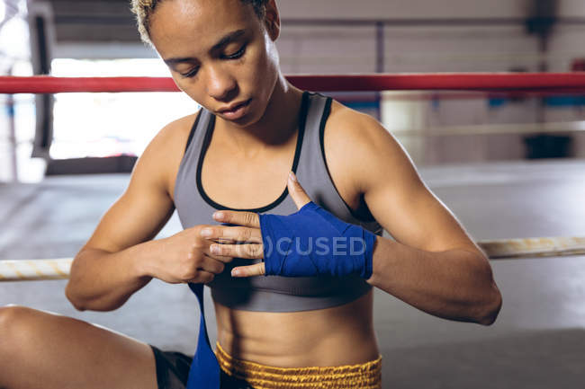 Вид спереди женщины-боксера в ручной упаковке в боксерском клубе. Сильная женщина-боец в боксёрском зале тяжело тренируется
. — стоковое фото