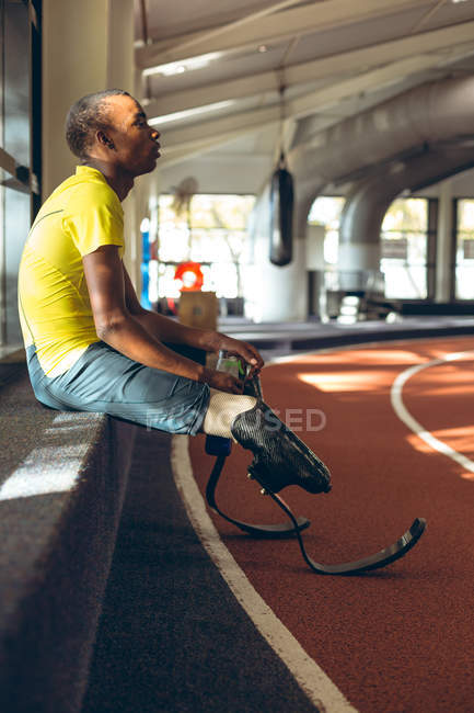 Vue latérale d'un athlète masculin afro-américain handicapé se relaxant dans un centre de fitness — Photo de stock
