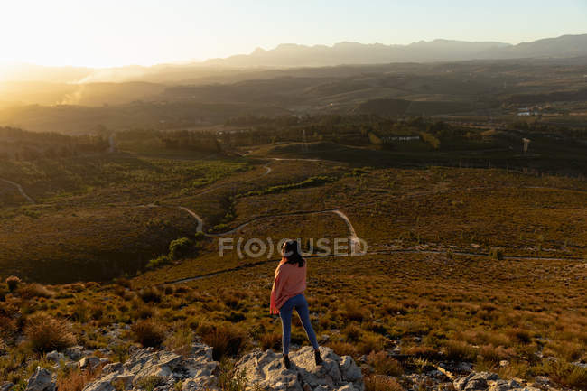 Вид ззаду на молоду жінку, що стоїть на скелі, насолоджуючись пейзажними пейзажами під час зупинки в дорожній поїздці . — стокове фото