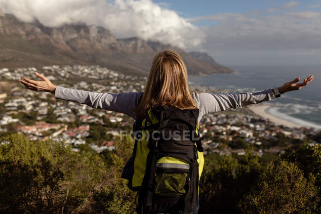 Rear view close up of a mature Caucasian woman wearing a backpack standing with arms outstretched enjoying the view during a hike. — Stock Photo