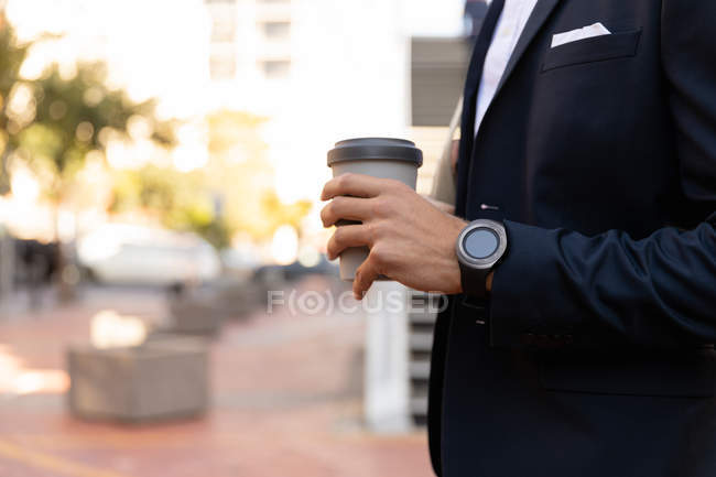 Side view mid section man wearing a jacket standing on a city street holding a takeaway coffee. Digital Nomad on the go. — Stock Photo