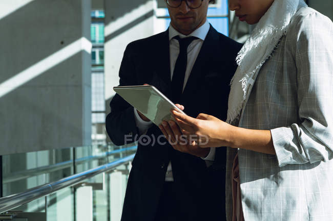 Средняя группа деловых людей, работающих вместе над цифровым планшетом в коридоре в современном офисе . — стоковое фото