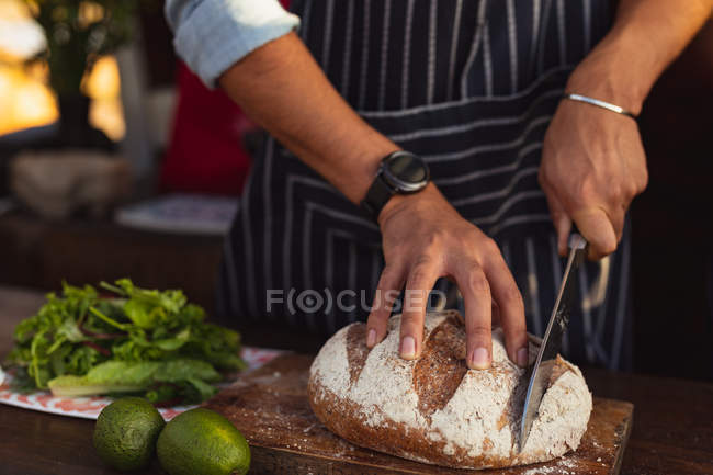 Вид спереди на человека в фартуке, режущего хлеб в фургоне с едой — стоковое фото