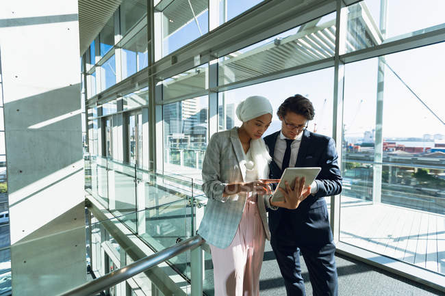 Frontansicht von Geschäftsleuten, die im Flur eines modernen Büros gemeinsam an einem digitalen Tablet arbeiten. — Stockfoto
