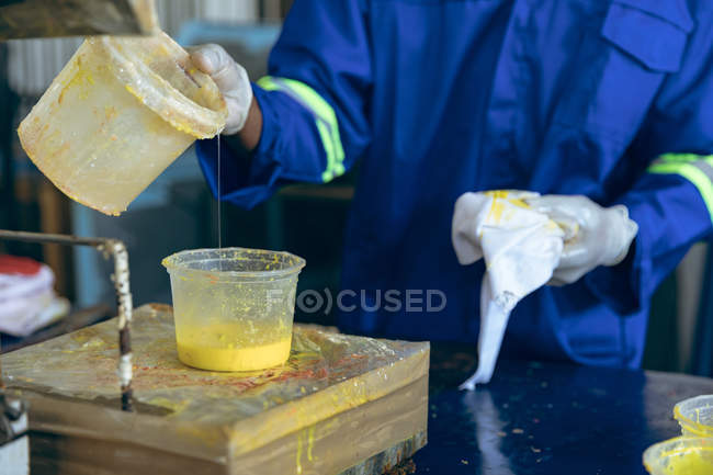 Vue de face section médiane de l'homme travaillant dans une usine de balles de cricket versant du caoutchouc jaune dans un récipient en plastique — Photo de stock