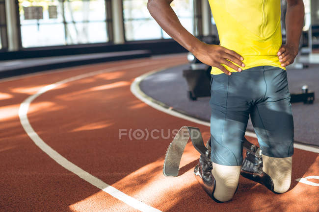 Close-up of disabled male kneeling with hands on hip in fitness center — Stock Photo