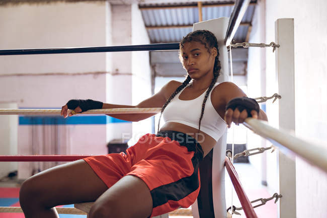 Portrait of female boxer relaxing in boxing ring at fitness center. Strong female fighter in boxing gym training hard. — Stock Photo
