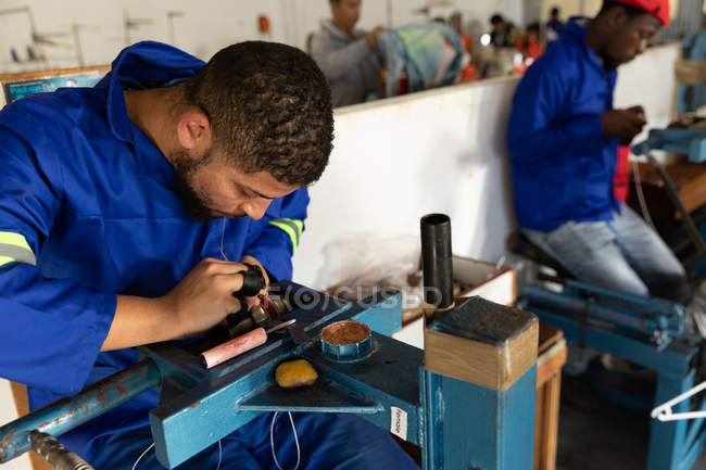 Side view close up of a young mixed race man sitting at a machine working in a workshop at a factory making cricket balls — Stock Photo