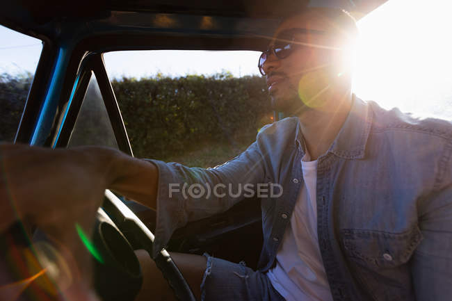 Vista laterale da vicino di un giovane uomo di razza mista sorridente seduto al volante di un pick-up che guida durante un viaggio su strada — Foto stock