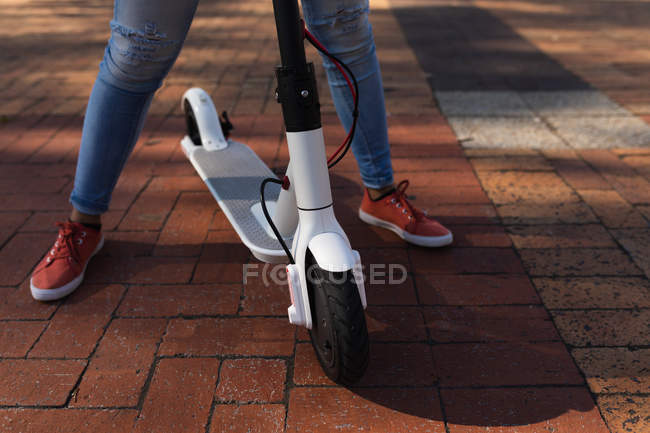 Вид спереду низька частина жінки, що стоїть на вулиці з електричним скутером — стокове фото