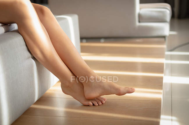 Nahaufnahme der Beine einer Frau, die auf einem Sofa im Sonnenlicht sitzt. — Stockfoto