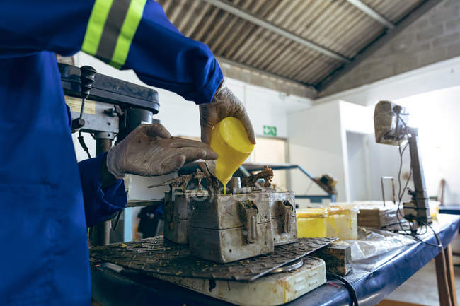 Side view mid section of man working at a cricket ball factory pouring yellow rubber into a mould. — Stock Photo