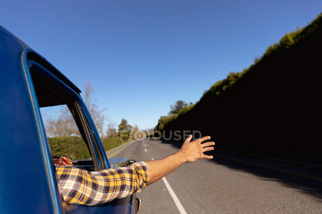 Вид сзади на человека с рукой, торчащей из бокового окна пикапа, когда он едет по шоссе в дорожное путешествие — стоковое фото