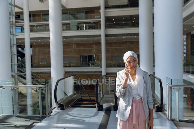 Vista frontale della donna d'affari in hijab che parla sul cellulare in un ufficio moderno . — Foto stock