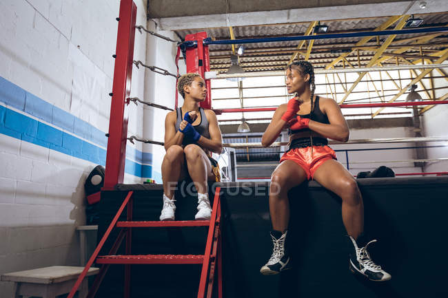 Вид спереду на жінок-боксерів, які розмовляють і носять ручну обгортку в боксерському клубі. Сильний жіночий боєць в тренажерному залі боксу важко . — стокове фото