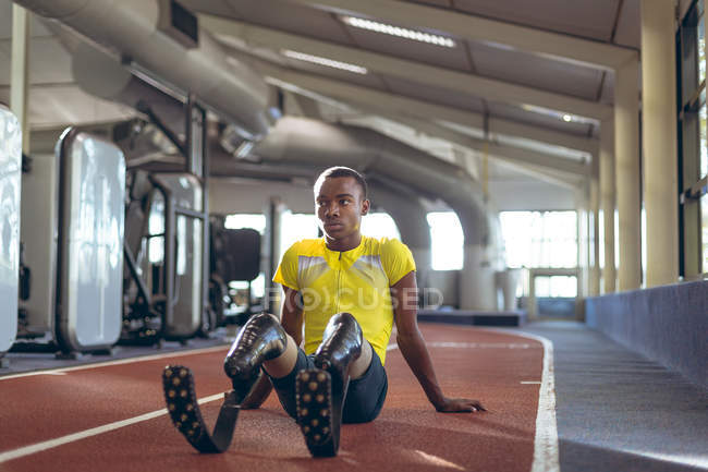 Vista frontal del atlético masculino discapacitado relajándose en una pista de atletismo en el gimnasio - foto de stock