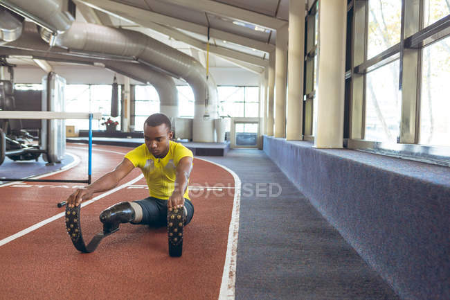 Vista frontal de los hombres afroamericanos discapacitados haciendo ejercicio en pista de atletismo en el gimnasio - foto de stock