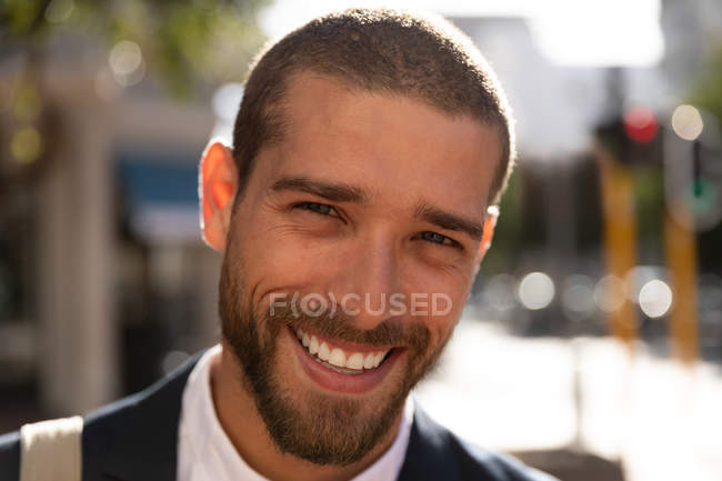Портрет улыбающегося молодого кавказца, стоящего на солнечной городской улице. Цифровая реклама на ходу . — стоковое фото