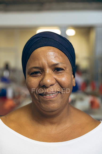 Retrato close-up de uma mulher de meia-idade mista em uma fábrica de roupas esportivas, olhando para a câmera e sorrindo . — Fotografia de Stock