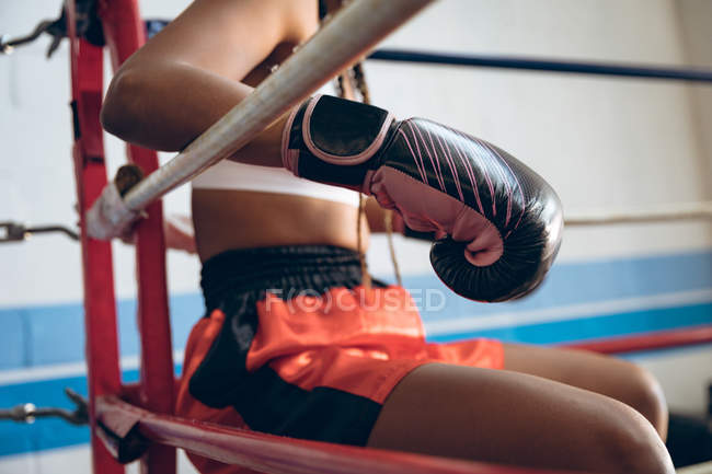 Close-up of female boxer relaxing in boxing ring at fitness center. Strong female fighter in boxing gym training hard. — Stock Photo
