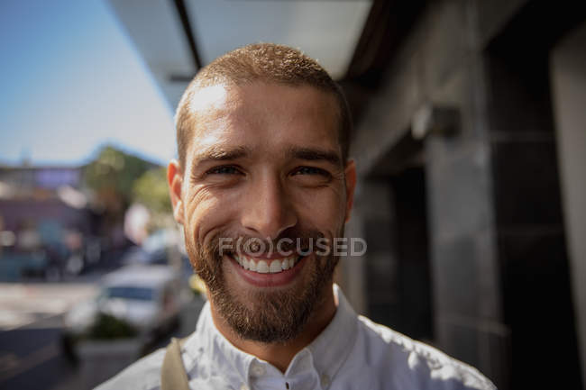 Portrait close up of a young Caucasian man in a city street and smiling to camera. Digital Nomad on the go. — Stock Photo