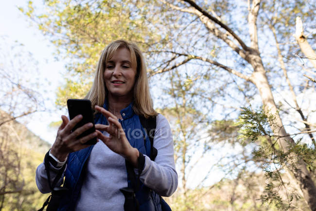Nahaufnahme einer reifen kaukasischen Frau, die während einer Wanderung ein Smartphone benutzt — Stockfoto