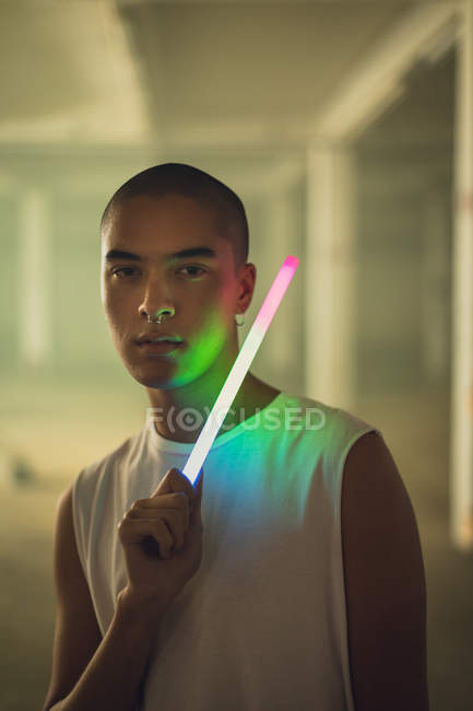Front view of a young Hispanic-American man with piercing on both ears and nose wearing a white sleeveless holding a light stick looking intently at the camera — Stock Photo