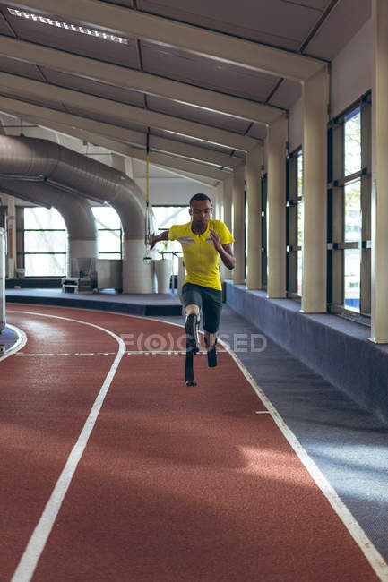 Vista frontal do atlético masculino afro-americano deficiente correndo em pista de esportes no centro de fitness — Fotografia de Stock