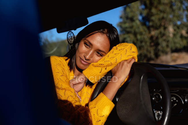 Портрет крупним планом молодої змішаної жінки, що спирається на кермо пікапа, посміхається, під час зупинки в дорожній поїздці — стокове фото