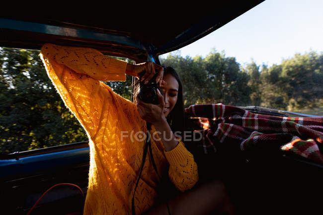 Close up of a young mixed race woman sitting in the front passenger seat of a pick-up truck taking photos with a camera during a road trip — Stock Photo