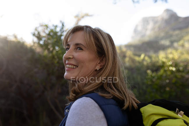 Side view close up of a mature Caucasian woman wearing a backpack turning her head and looking up at the scenery during a hike. — Stock Photo