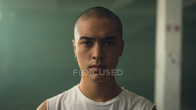 Vista de cerca de un joven hispano-americano con piercing en ambas orejas y nariz llevando una manga blanca mientras mira atentamente a la cámara - foto de stock