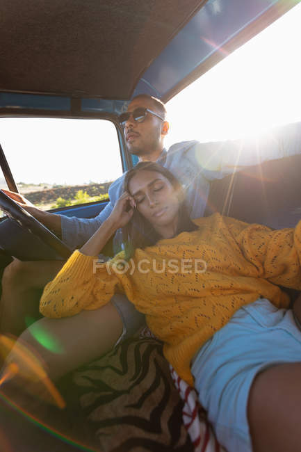 Close up low angle view of a young mixed race couple sitting in their pick-up truck during a road trip. The man is driving and the woman is leaning on him with her eyes closed — Stock Photo
