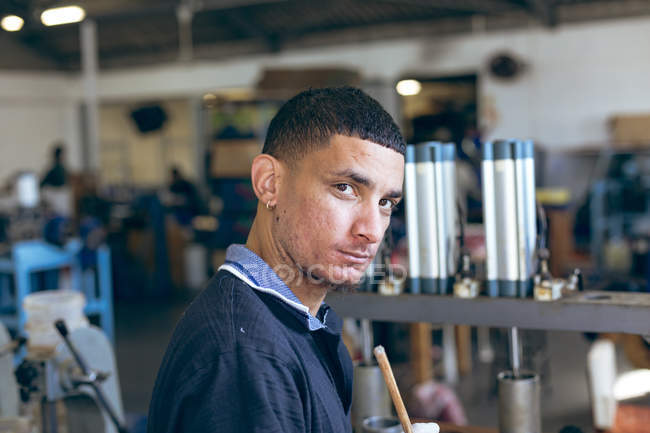 Porträt eines jungen gemischten Rennfahrers, der in einer Sportgerätefabrik arbeitet, sich umdreht und in die Kamera blickt. — Stockfoto