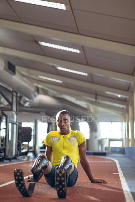 Vue de face d'un athlète masculin handicapé se relaxant sur une piste de course dans un centre de fitness — Photo de stock