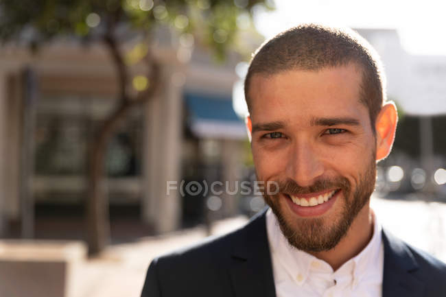 Porträt eines lächelnden jungen kaukasischen Mannes, der auf einer sonnigen Straße der Stadt steht. Digitaler Nomade unterwegs. — Stockfoto