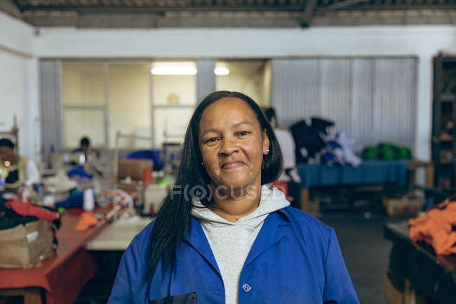 Portrait close up of a middle aged mixed race woman in a sports clothing factory, looking to camera and smiling. — Stock Photo