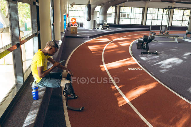 Side view of disabled African American male athletic using mobile phone in fitness center — Stock Photo