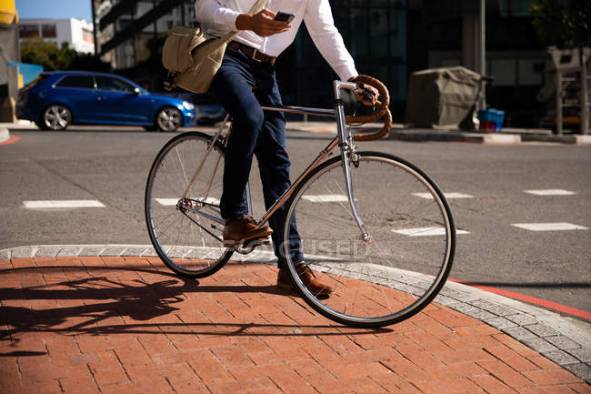 Vorderansicht eines Mannes mit Smartphone, der auf seinem Fahrrad in einer Straße in der Stadt sitzt. Digitaler Nomade unterwegs. — Stockfoto