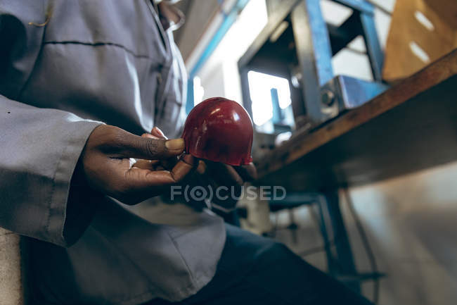 Вид сбоку средняя секция мужчины работника сидя и держа форму красный кожаный чехол мяч на заводе, делающий крикетные шары . — стоковое фото