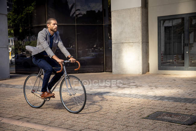 Vista laterale di un giovane caucasico in bicicletta in una strada della città. Nomade digitale in movimento . — Foto stock